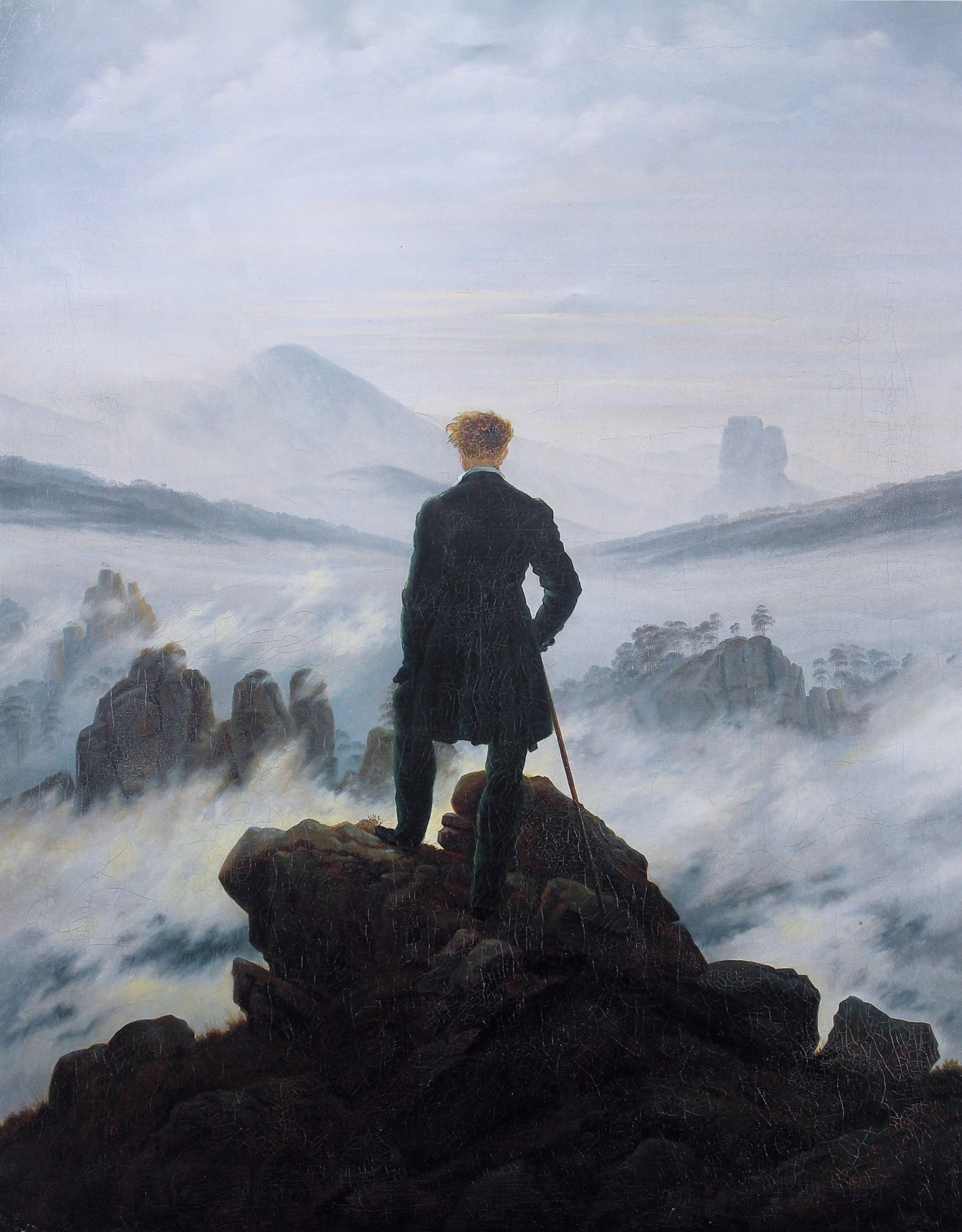 A man seen from behind, standing on a rocky peak above a misty landscape.